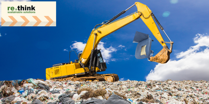 A digger working at a landfill site with a broken office chair and waste